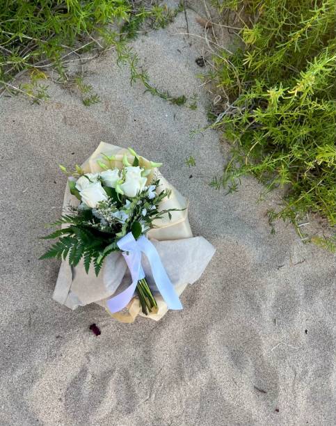 A beautiful bouquet of vibrant flowers on the sand of Secret Beach, Oahu, Hawaii. This image captures the contrast between the delicate floral arrangement and the natural tropical setting, evoking a sense of tranquility and elegance. Ideal for themes related to beach weddings, romantic getaways, and coastal decor, showcasing the beauty of flowers in a beachside environment.