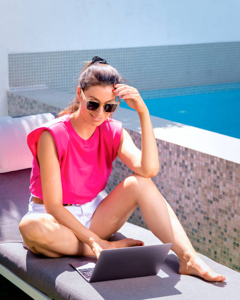 istock Happy woman sitting at pool and using her laptop 2167581550