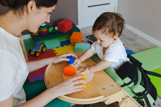 Little boy with movement disorders standing in a verticalizer during rehabilitation session with a physical therapist, spending time in a fun and healthy way