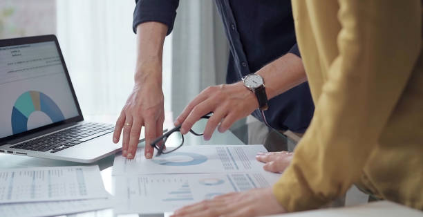 istock Business people, professionals analyzing financial charts and data on a desk while standing and using laptop computer in office. Dark blue shirt and yellow blouse 2167585534