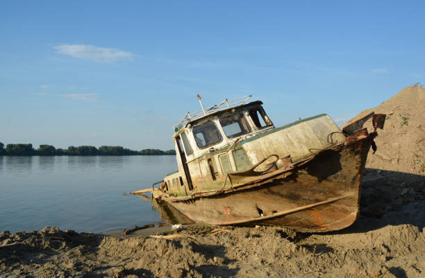 stranded wooden boat at Danube the river banks with blue river water, blue sky and a forest on the other side of a river.