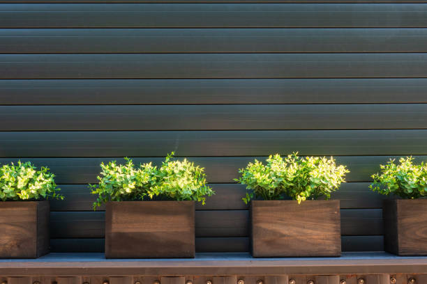 Artificial green plants in wooden boxes against closed brown roller shutter. Outdoor decor. Background.