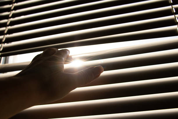 istock Woman's hand opens white blinds on window and lets sunlight 2167603623