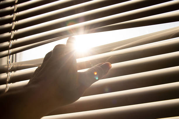 istock Woman's hand opens white blinds on window and lets sunlight 2167603632