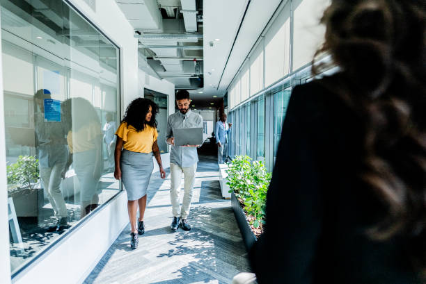 istock Coworkers talking and using laptop while walking through the office 2167605571