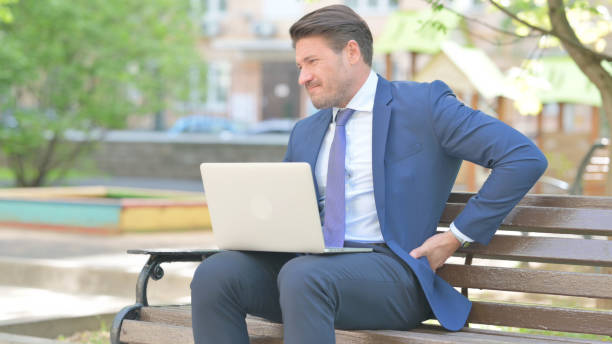 istock Businessman with Back Pain Using Laptop while Sitting Outdoor on Bench 2167608929