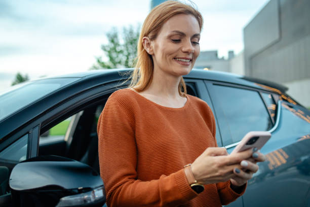 istock Casual woman using smart phone while standing by her car 2167614634
