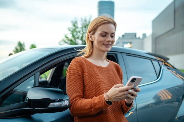 istock Casual woman using smart phone while standing by her car 2167614638