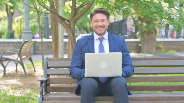 istock Middle Aged Businessman Smiling at Camera while Using Laptop Outdoor 2167616132