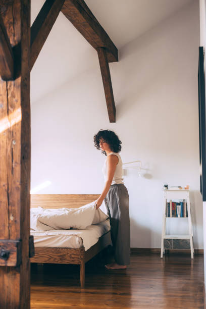 istock Woman Making Bed in Cozy Sunlit Bedroom Interior 2167617414