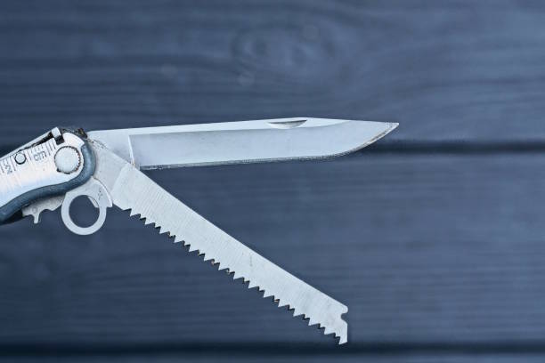 part of grey metal multitool with knife and saw on black background