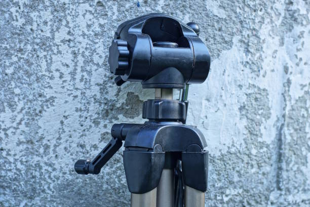 it is a black plastic tripod head on a brown metal stand against a grey concrete wall outside