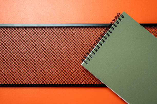 A green spiral notebook sits on top of a black metal frame. The notebook is open to a blank page, ready for writing