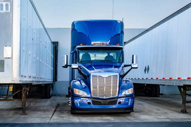 istock Bright blue big rig semi truck tractor standing between two loading semi trailers in warehouse dock gates 2167664677