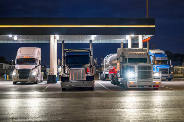 istock Big rigs semi-trucks with different semi trailers parked for truck driver rest under a lighted covered shelter on truck stop parking lot at night time 2167664860