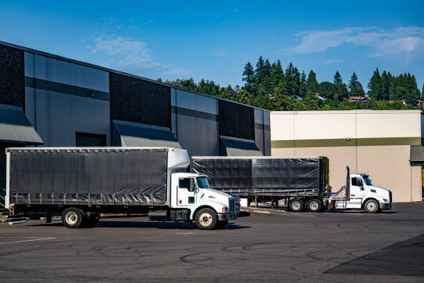 istock Day cab white big rig semi trucks with Conestoga trailers loading cargo standing in warehouse dock gates 2167664900
