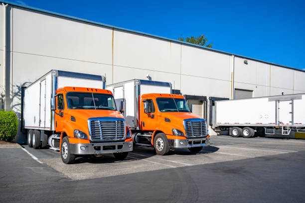 istock Orange middle duty day cab rigs semi trucks with box trailers loading cargo standing side by side in warehouse dock gates 2167665300