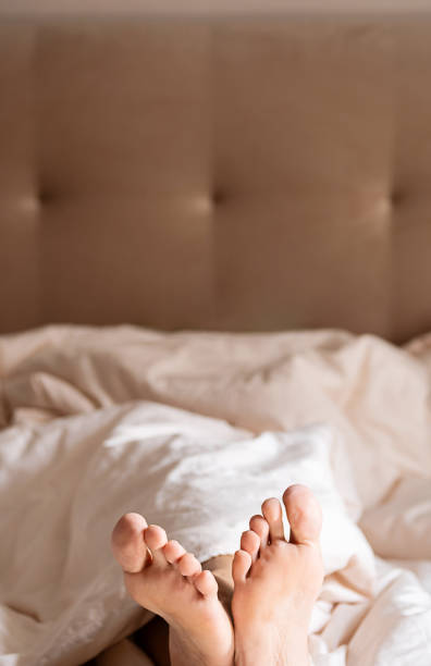 Bare feet peeking out from under blanket on bed.