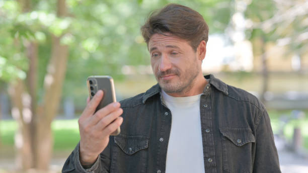 istock Middle Aged Man Doing Video Chat on Phone Outdoor 2167685965