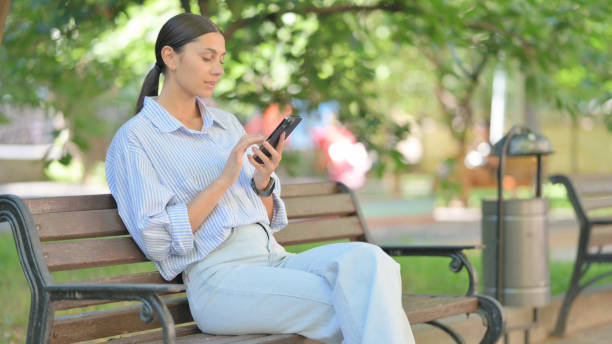 istock Mixed Race Woman Using Smartphone while Sitting Outdoor 2167688108