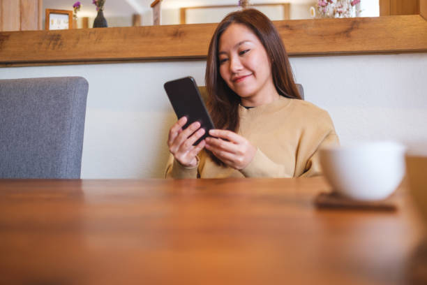 istock Portrait image of a young woman holding and using mobile phone while drinking coffee in cafe 2167697888