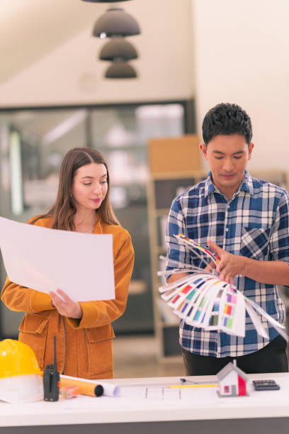istock Two male and female architects designing a construction project on blueprints and a house model standing in the office are talking about placing a real estate business girlfriend. 2167703470