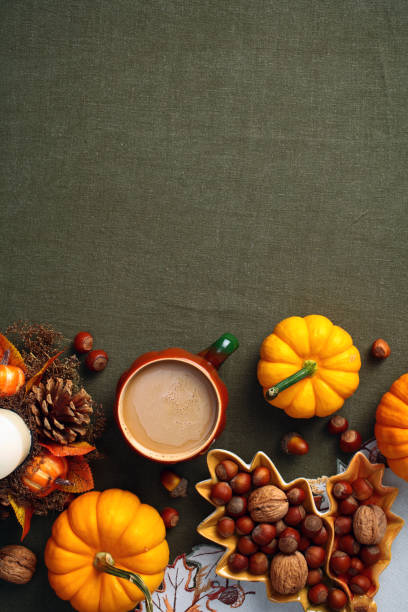 istock Autumn flat lay composition with pumpkins, coffee cup, candle, maple leaf shaped plate with nuts on green textile background. Autumn hygge style desk table, top view. 2167703474