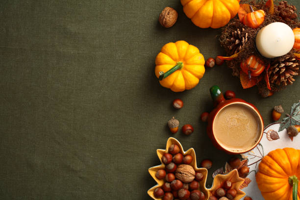 istock Autumn desk top view. Flat lay composition with pumpkins, coffee cup, maple leaf shaped plate with nuts, candle on green table cloth. 2167703653
