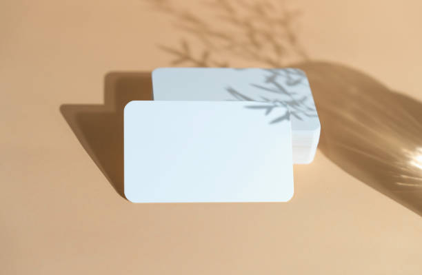 White Business Card Mockup with Glass and Leaf Shadows Reflecting on a Simple Background.