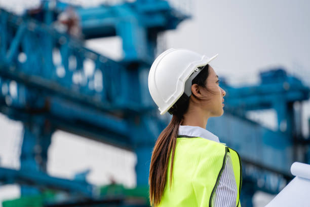 istock Construction workers wearing a yellow vest standing in front of a large blue crane. 2167708377