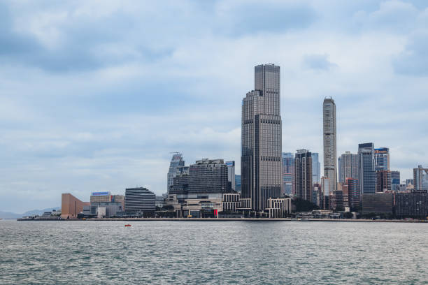 A sweeping panorama reveals Hong Kong's skyline with towering skyscrapers against a backdrop of overcast sky and tranquil waters.