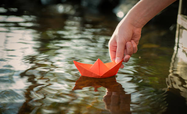 istock a boy puts a paper boat into the water 2167727379