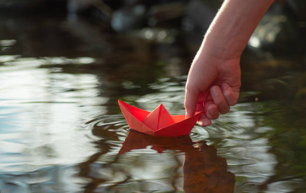 istock a boy puts a paper boat into the water 2167727391
