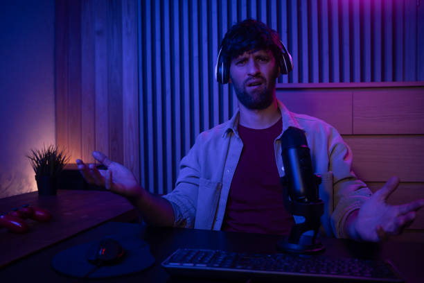 A gamer is actively participating in a live streaming session while speaking into a microphone. The setting features a stylish, dimly lit room with colorful lighting, creating an engaging atmosphere for viewers. stock photo
