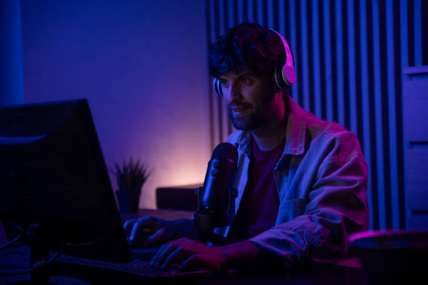 istock A young man is engaged in an intense gaming session while streaming live. He sits at a desk with a computer, wearing headphones and speaking into a microphone, creating an inviting atmosphere with vibrant lighting in the background. 2167736794