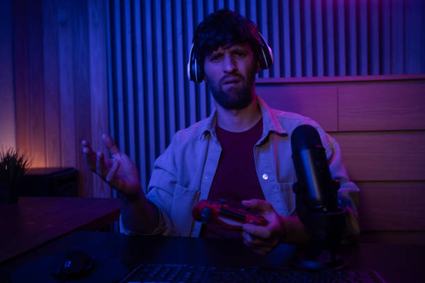 istock A gamer is fully immersed in an engaging session while holding a controller. The room is illuminated with colorful lighting, creating a vibrant atmosphere. The microphone positioned nearby captures every moment of excitement and commentary. 2167736967