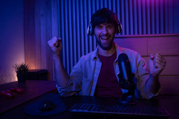 istock A gamer is actively participating in a live streaming session while speaking into a microphone. The setting features a stylish, dimly lit room with colorful lighting, creating an engaging atmosphere for viewers. 2167737161