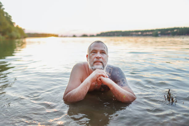 mature man swims in a lake at sunset
