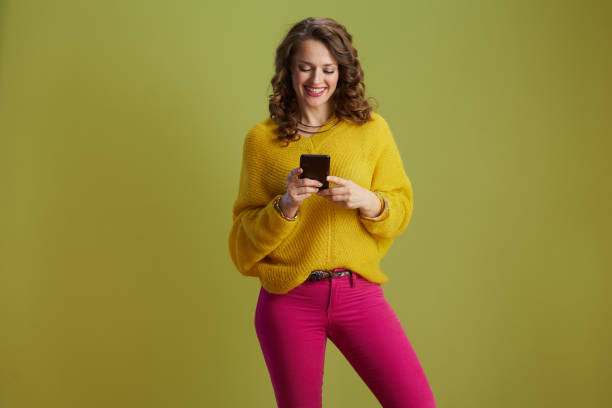 istock smiling trendy woman using smartphone isolated on green 2167739517