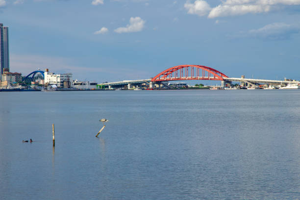 Sokcho, South Korea - July 28th, 2024: A scenic view of the Seorak Grand Bridge with its vibrant red arches spanning over Cheongcho Lake, connecting the city's waterfront under a calm sky, with modern buildings visible in the distance.