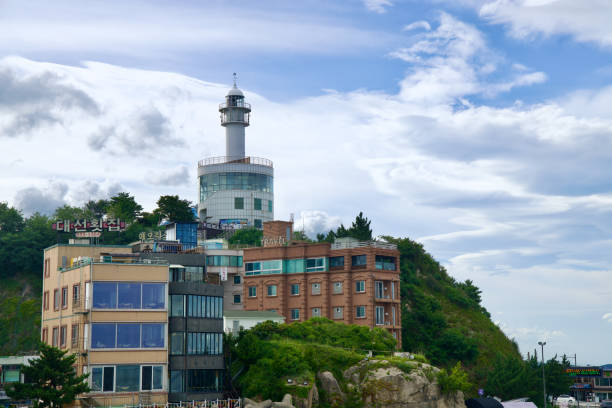 Sokcho, South Korea - July 28th, 2024: Sokcho Lighthouse rises prominently above the surrounding buildings and greenery, as seen from Yeonggeum Sunrise Pavilion. The modern lighthouse offers panoramic views of the East Sea and Sokcho's landscape.