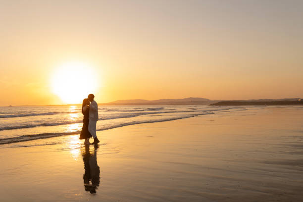 A couple is walking on the beach at sunset