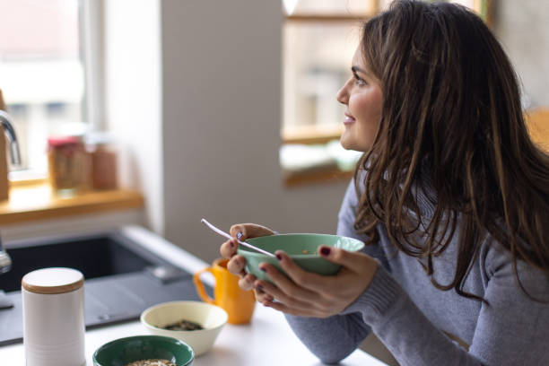istock Young woman using her phone while eating breakfast at home 2167752864