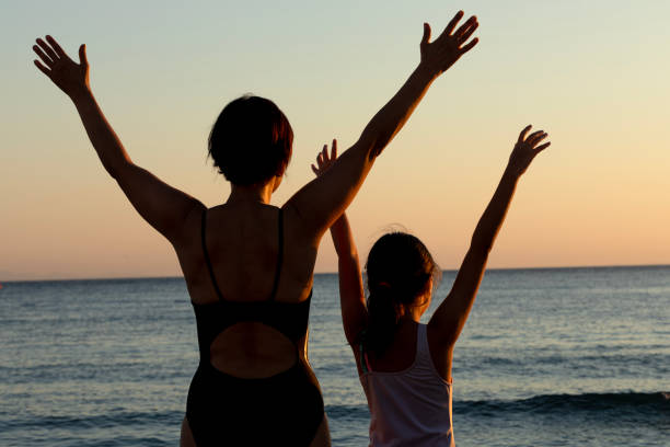 Mother and daughter are watching the sun set in the sea.