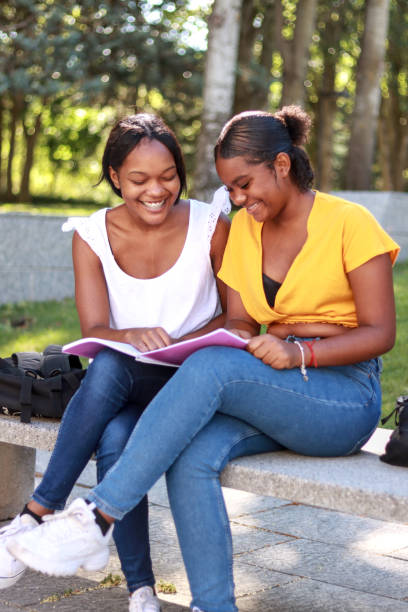 istock Two young Hispanic women sitting on a park bench, studying together from a shared notebook 2167761637