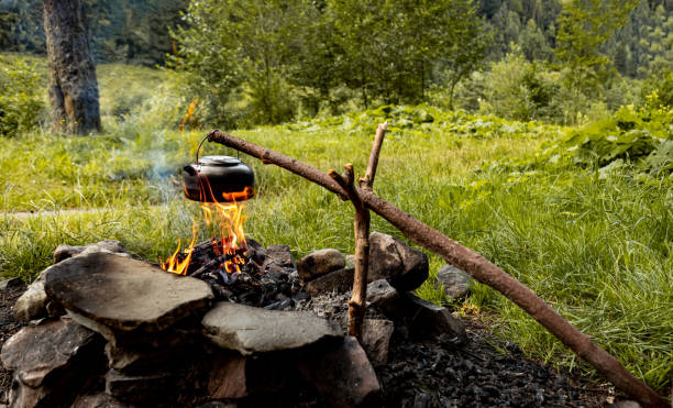 Making tea over an open fire in the forest. The kettle is hanging on a stick on the fire.