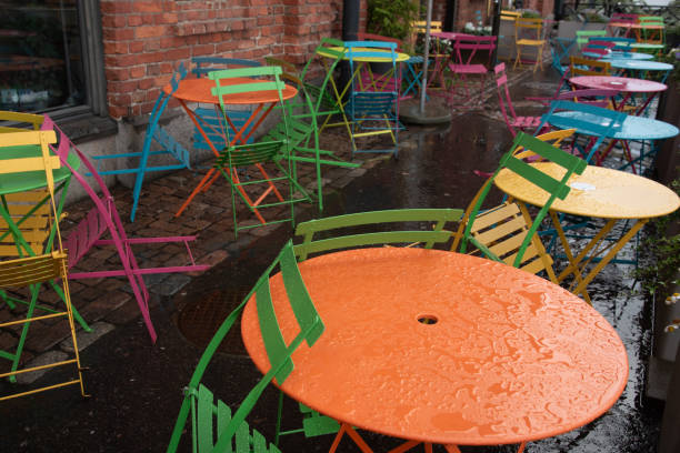 istock Multiple empty yellow orange blue colored metal round tables and chairs at a bistro cafe on a restaurant sidewalk patio during rain 2167765123
