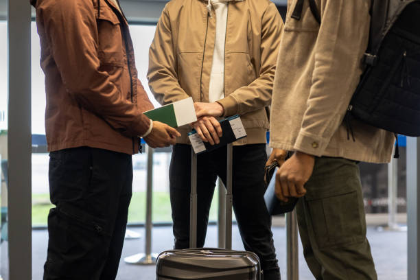Side midsection view of unrecognisable tourists and travellers waiting in line to check in with their boarding passes for their flight at the desk. They are waiting for the attendant that is out of the shot to check their tickets and allow them to board the flight.