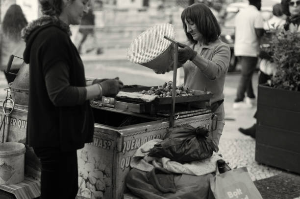 Lisbon, Portugal - November 11, 2023: A couple of traditional roasted chestnuts vendors, prepare the roasted chestnuts at the Rua Augusta street in Lisbon downtown.