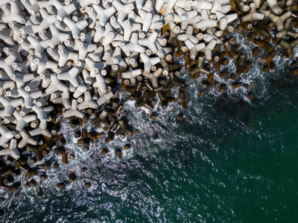 istock Aerial view of concrete tetrapod wave breakers along a rugged shoreline, with waves crashing against them, creating a dynamic and textured seascape. Ideal for coastal, industrial, and nature themes 2167776098